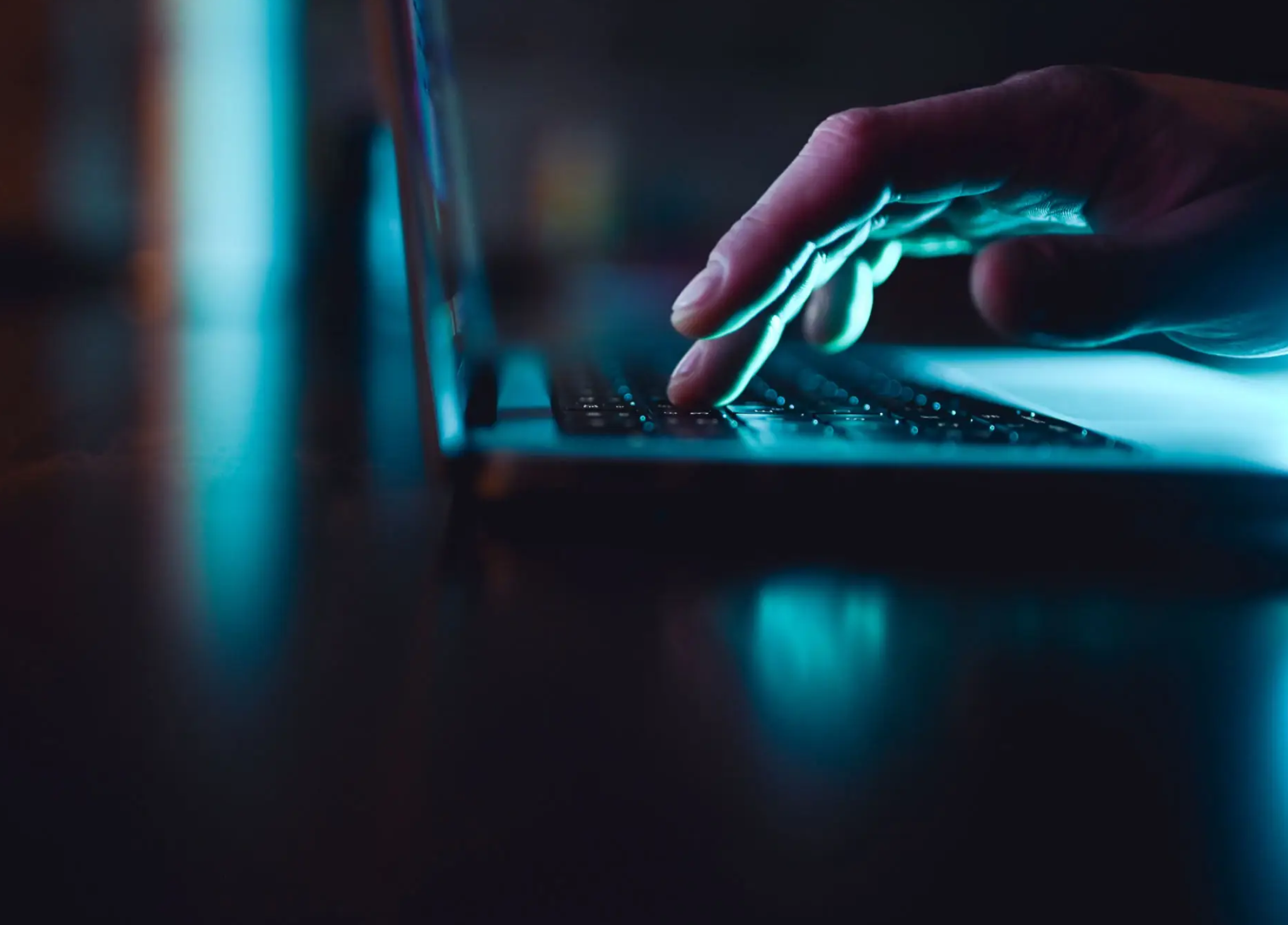 Close-up of fingers typing on backlit laptop